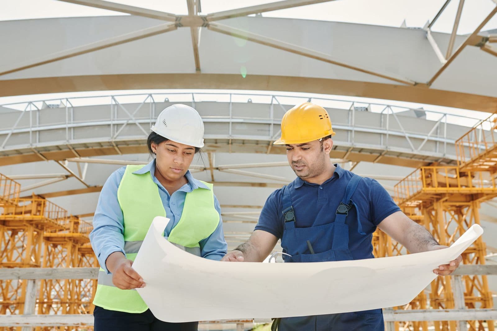 Two engineers in hard hats reviewing a drawing on a steel-structure site