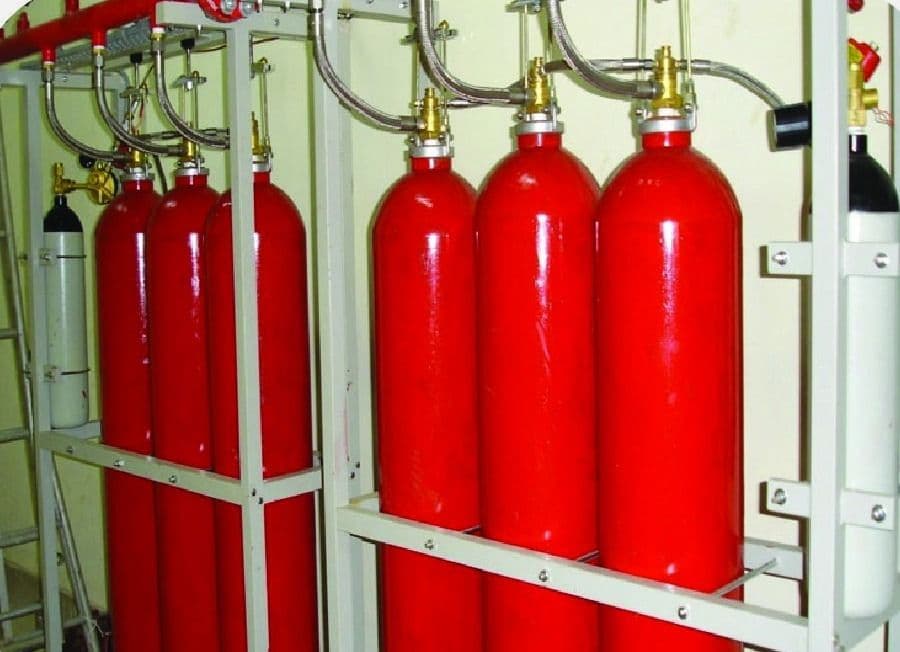 Bank of CO₂ cylinders with flexible discharge hoses and pilot cylinders