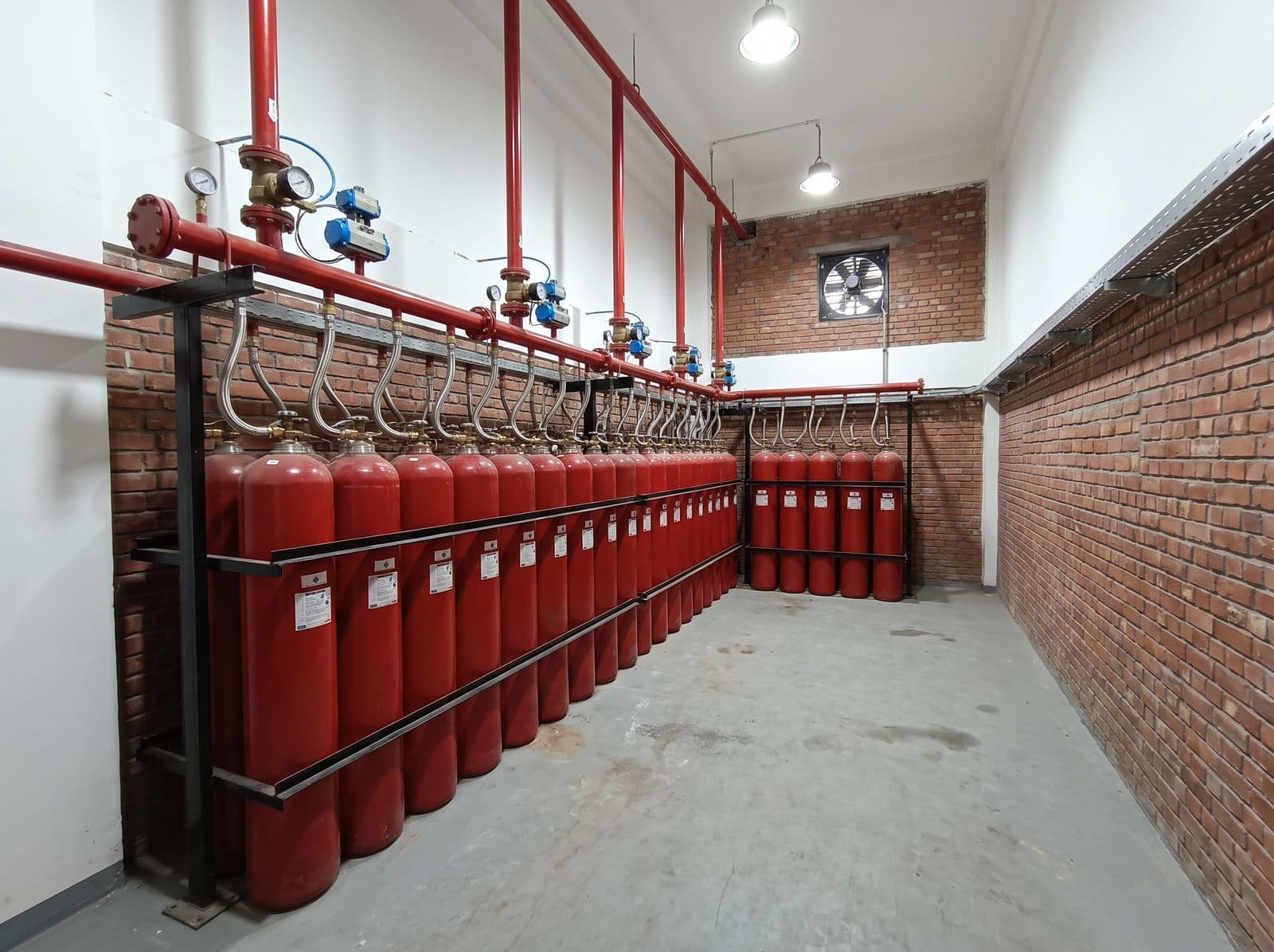 Inert gas cylinder banks with discharge manifold and selector valves in a cylinder room